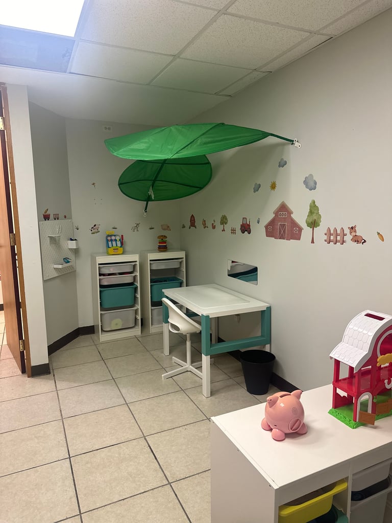 Bright childrens playroom with green leaf canopy, storage units, small table and chairs, farm wall decals, and toy vehicles