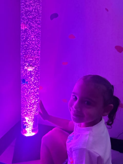 Child in white shirt interacting with a glowing purple cylindrical light tube in a purple-lit room