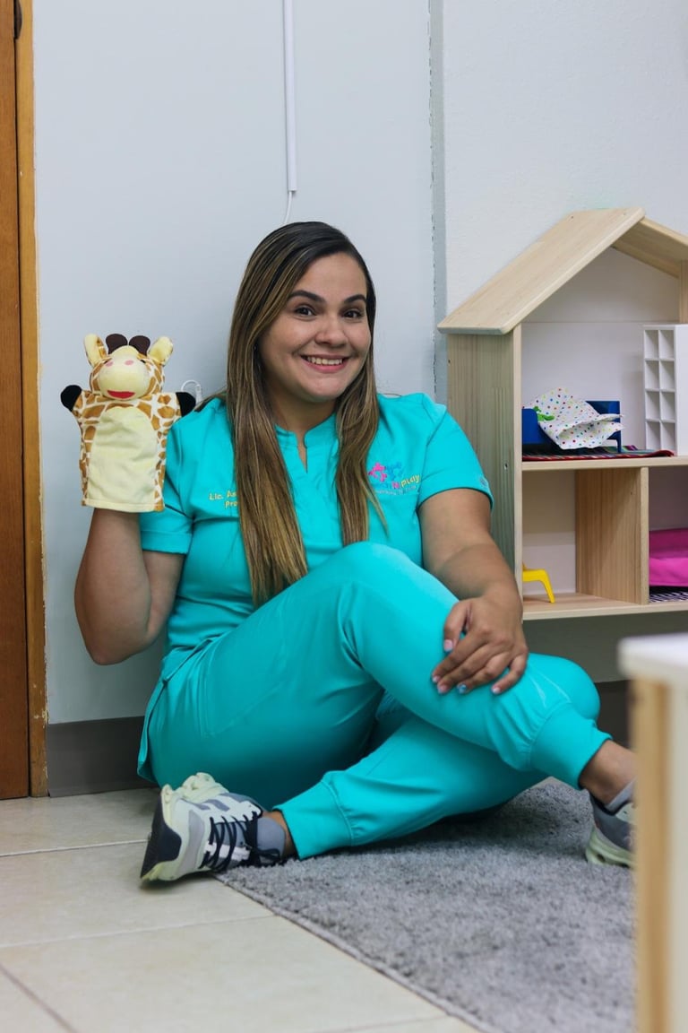 Woman in turquoise outfit sitting on floor holding a giraffe puppet in a playroom setting