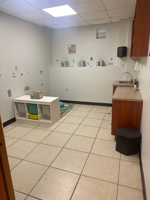 Daycare or classroom room with beige tile floor, storage cubby shelving, sink counter, and colorful educational materials on walls