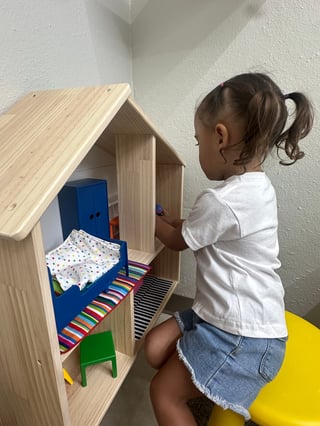 Child playing with wooden dollhouse containing miniature furniture and accessories against white wall